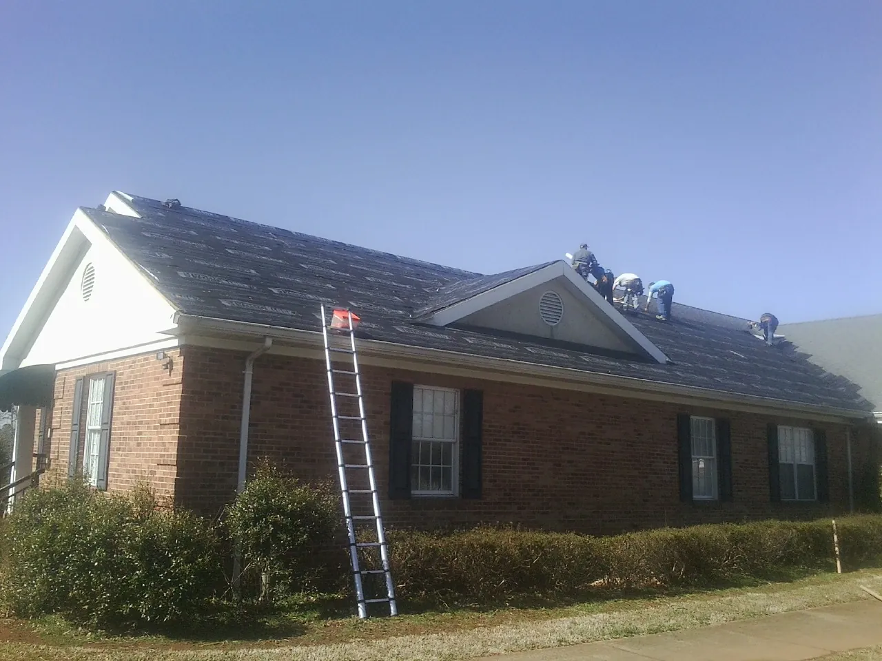 Crew tearing shingles off a brick ranch roof with a ladder set — Metal Roof Repair work by our crew in Modena