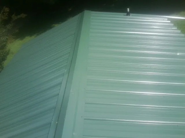 New green metal panels meeting at the ridge of a roof — Flat Roof Repair work by our crew in Modena