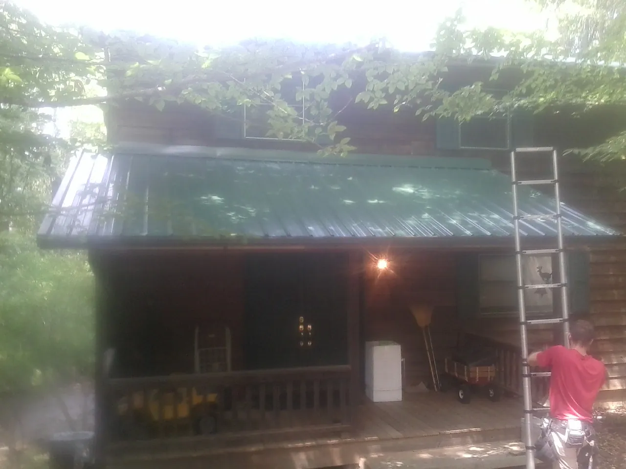 Worker on a ladder at the green porch roof of a wooded cabin in Modena